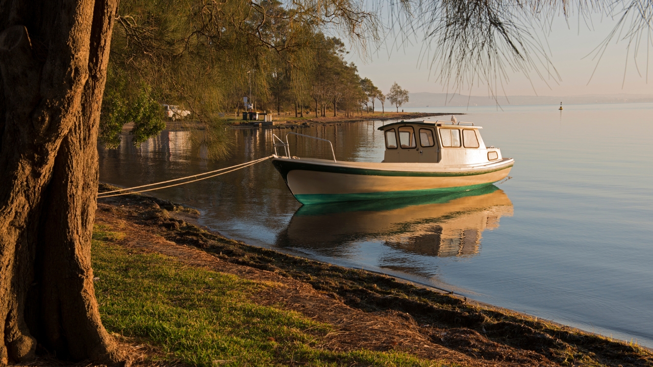Small white boat moored on calm lake water near grassy shoreline at Speers Point