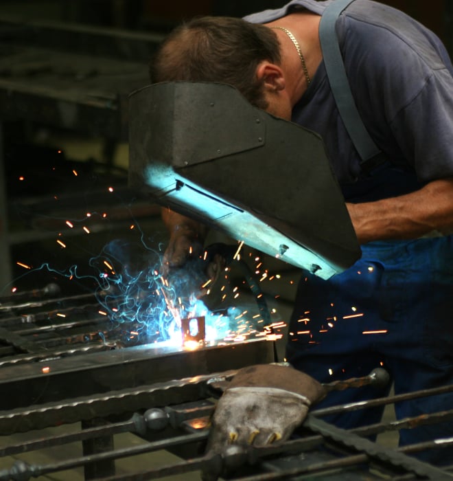 Welder wearing safety gear fabricating metal fencing in a workshop se