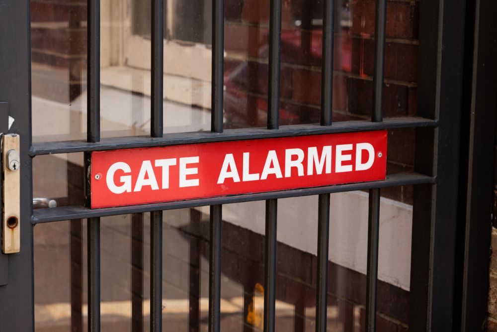 Alarmed steel gate with red warning sign installed by Chainwire Fencing Specialist for secure access