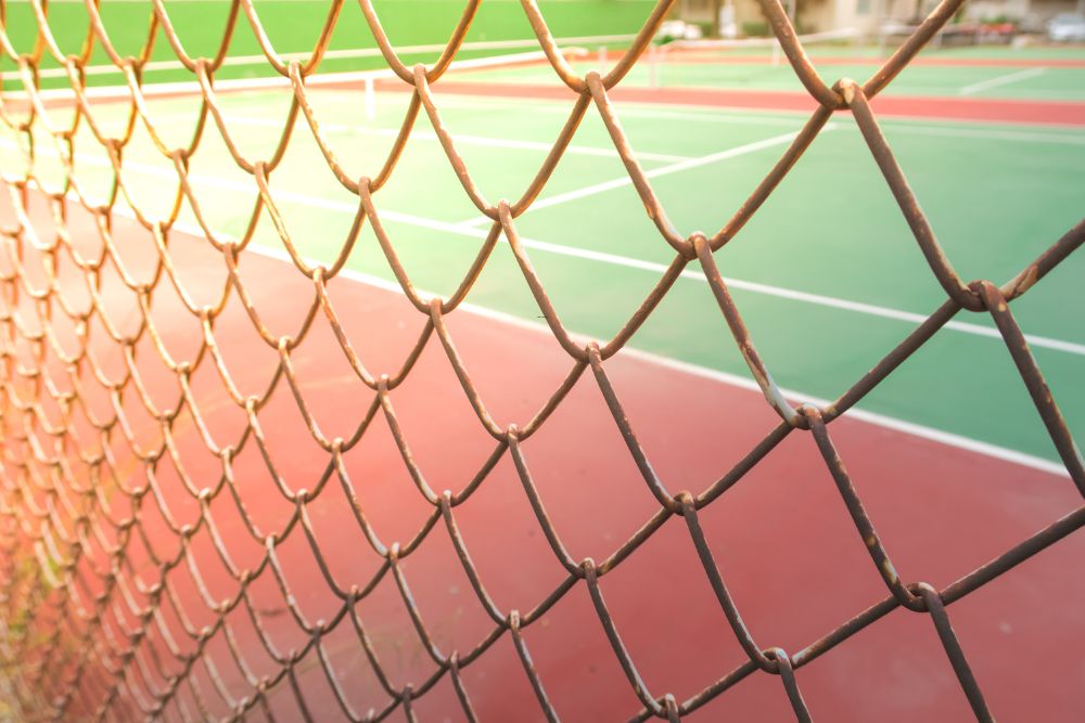 Chainwire fence surrounding red and green school sports court under late afternoon light