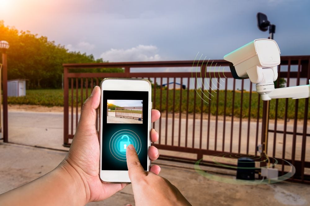 Person unlocking a security gate with smartphone while camera records access for Chainwire Fencing Specialist